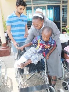 Italian Hospital Acting Administrator Sr. Ireen Kunda placing Philip Kusa, 4 years old and Chipata resident, in his newly donate wheel chair while looking on is Cardinal Distributors MD Safwaan Patel..